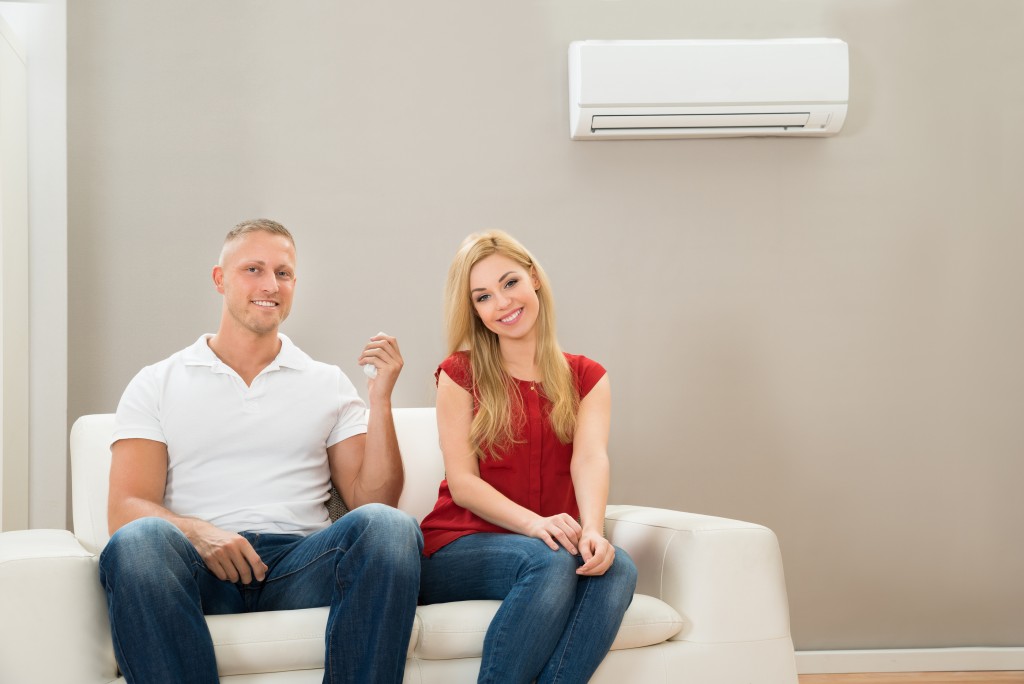 Young Happy Couple Sitting On Sofa Using Air Conditioner